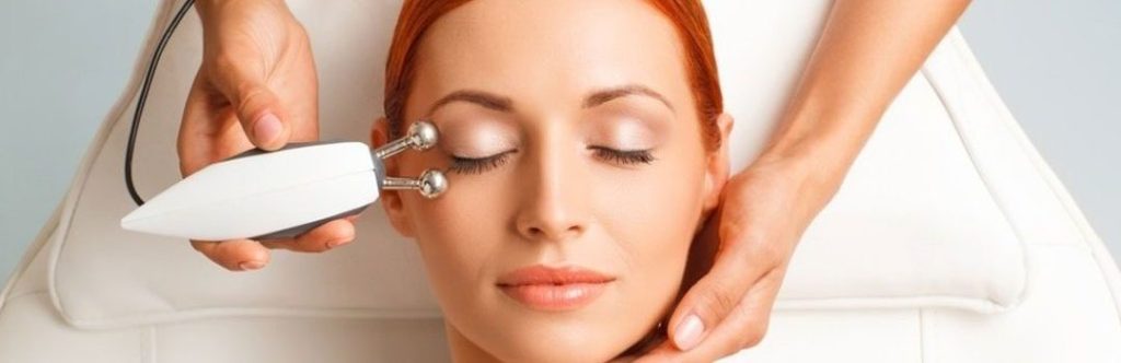 Red hair woman with closed eyes receiving microcurrent treatment at eye level